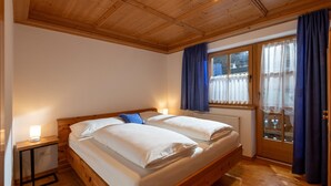 A double bed with white linens, a bedside table with a lamp, a window with blue curtains, and a wooden ceiling. - Apartment "Hans" with Mountain View, Balcony and Wi-Fi (Fügen)