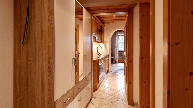 A narrow hallway with wooden walls and a tiled floor, leading to a kitchen area with wooden cabinets and a sink. - Apartment "Hans" with Mountain View, Balcony and Wi-Fi (Fügen)