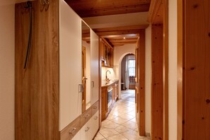 A narrow hallway with wooden walls and a tiled floor, leading to a kitchen area with wooden cabinets and a sink.