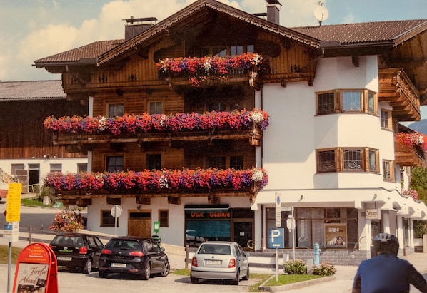 A multi-story wooden building with balconies adorned with flowers, a sign for 'Ost Gemuse,' and a parking sign.
