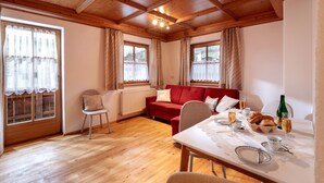 A room with a wooden ceiling, a red sofa, a dining table set with plates, glasses, and a bottle. - Apartment "Hans" with Mountain View, Balcony and Wi-Fi (Fügen)
