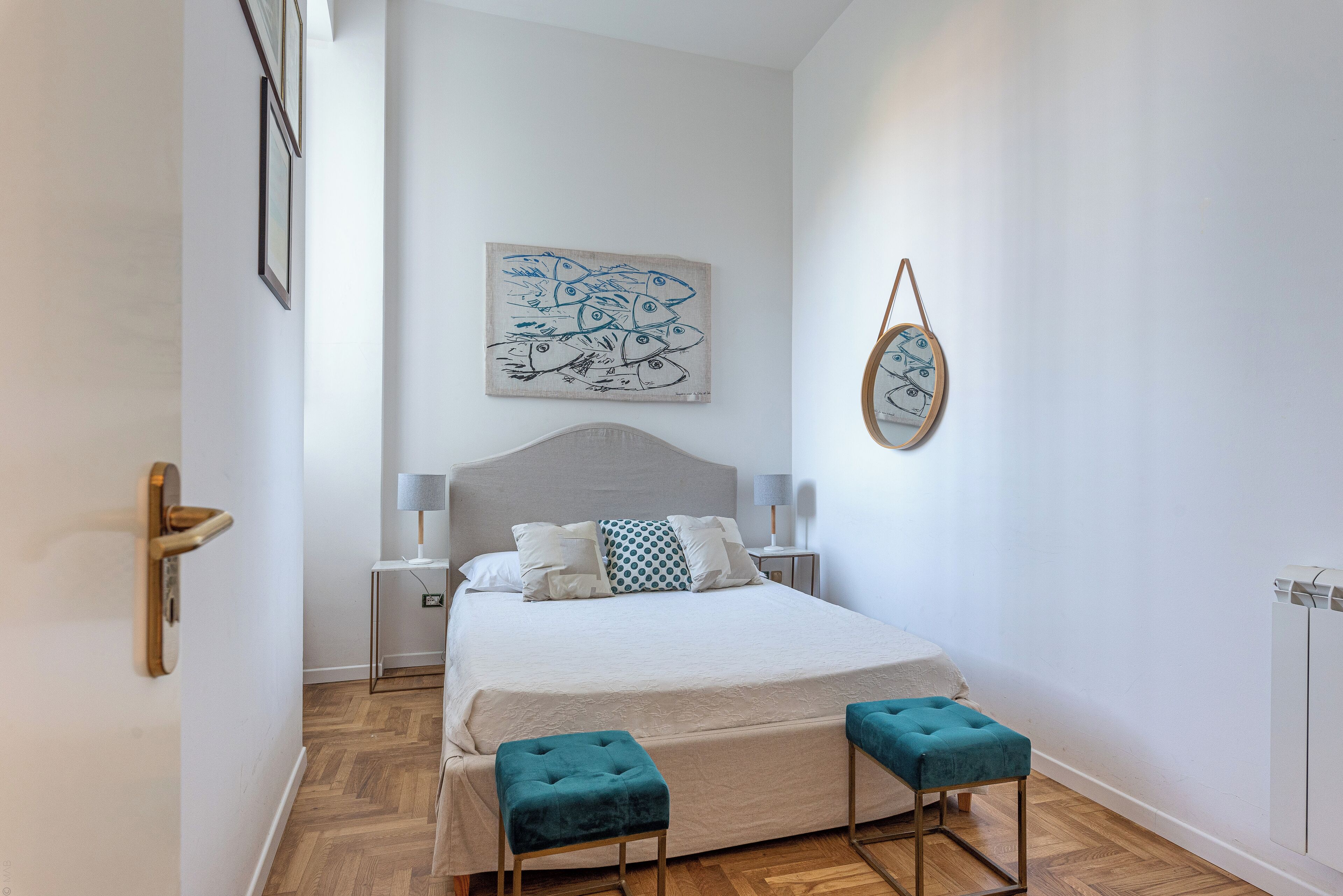 Un dormitorio con una cama, dos mesitas de noche, una obra de arte en la pared, un espejo y una puerta.
