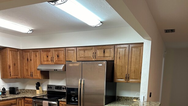 A kitchen with wooden cabinets, a stainless steel refrigerator, a granite countertop, and a built-in oven. - Marvelous 3-bedroom house located on a horse farm in Ocala minutes from WEC (Ocala)