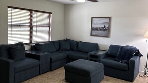 A living room with a sectional sofa, ottoman, ceiling fan, and a framed picture on the wall. - Marvelous 3-bedroom house located on a horse farm in Ocala minutes from WEC (Ocala)