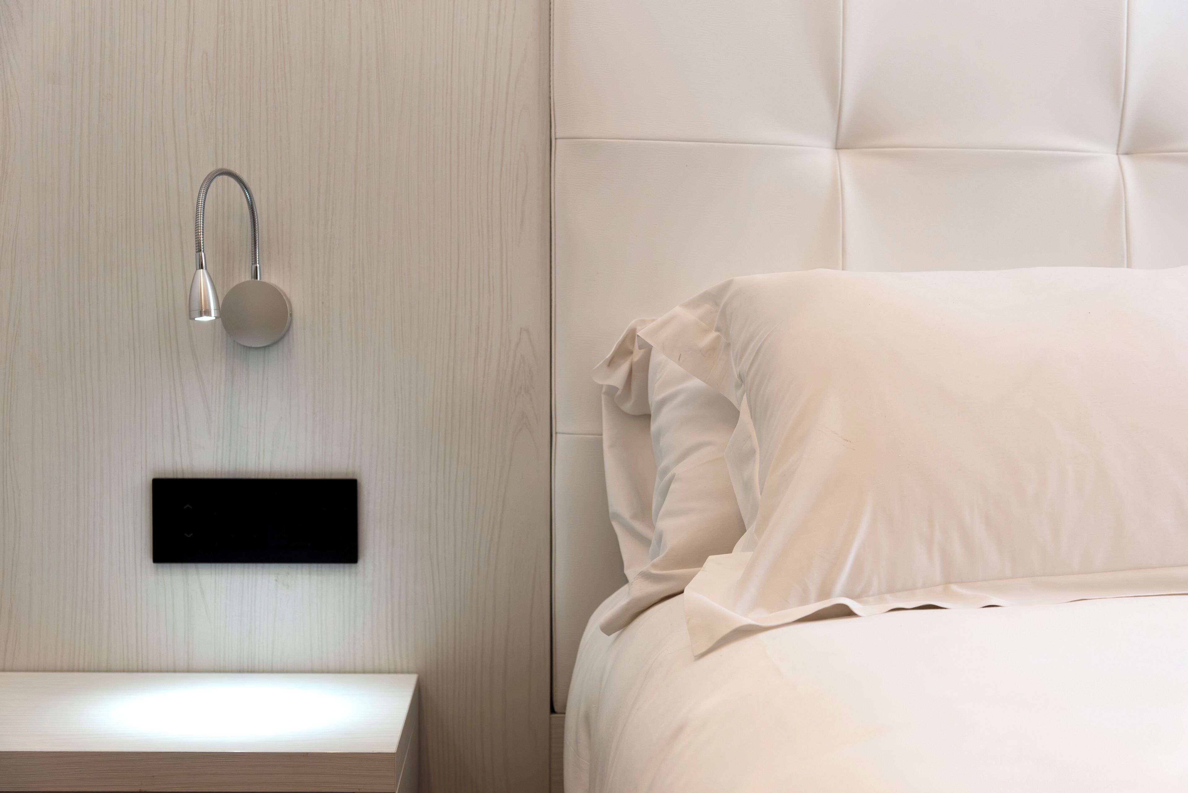 A modern bedroom with a headboard, a bedside table, and a wall-mounted light fixture.