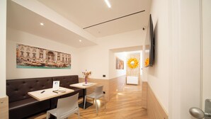 A modern hotel lobby with a wooden floor, a brown leather sofa, a small table with chairs, and a painting of a historical building. - Chessa's Rooms (Rome)