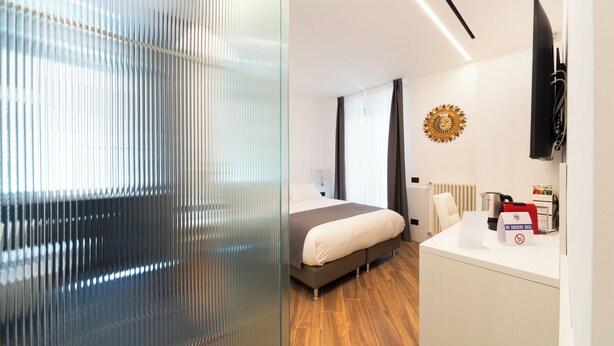 A modern hotel room with a large bed, a desk with a coffee machine, and a TV mounted on the wall. - Chessa's Rooms (Rome)