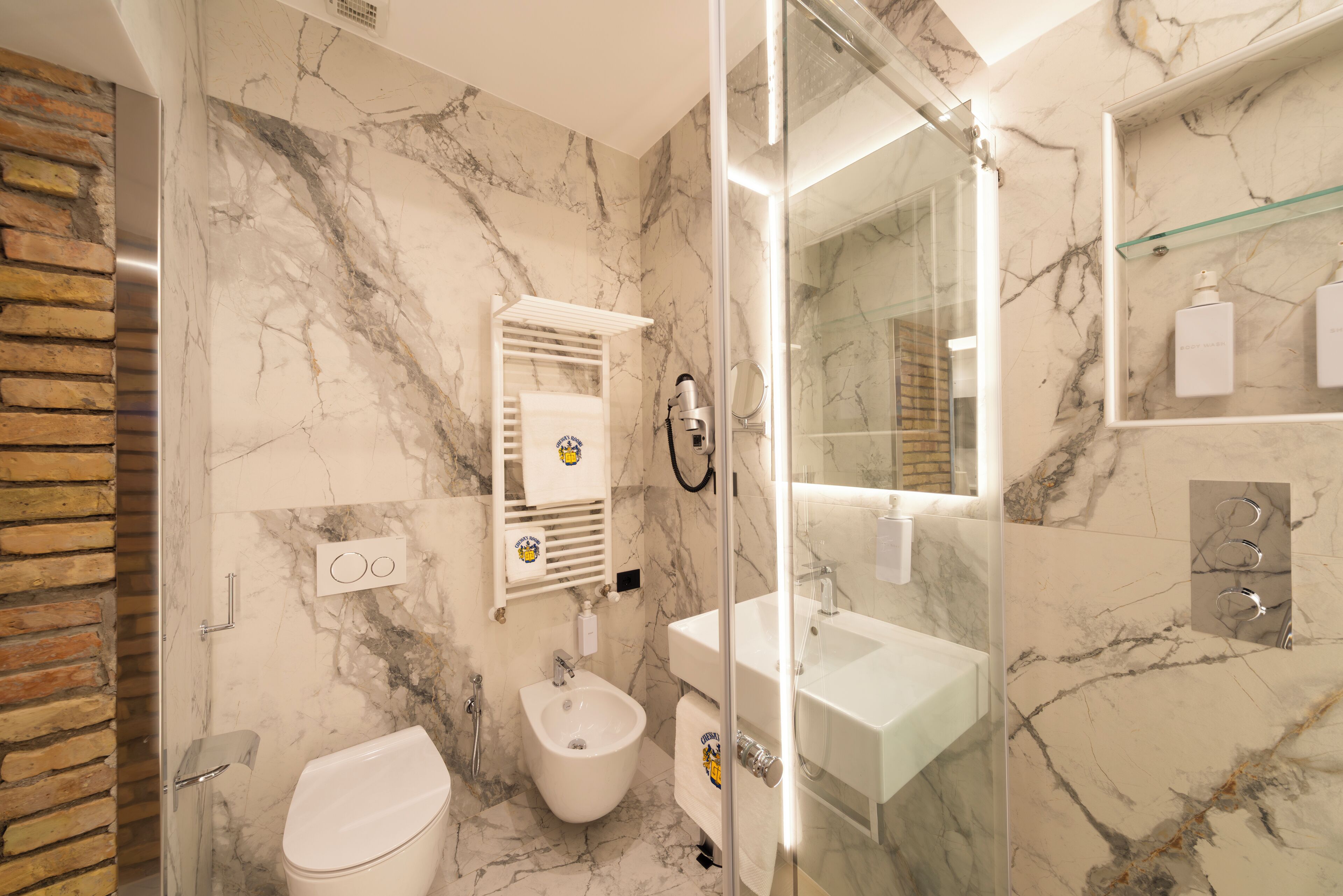 A bathroom with a bidet, a glass shower enclosure, and a marble wall.