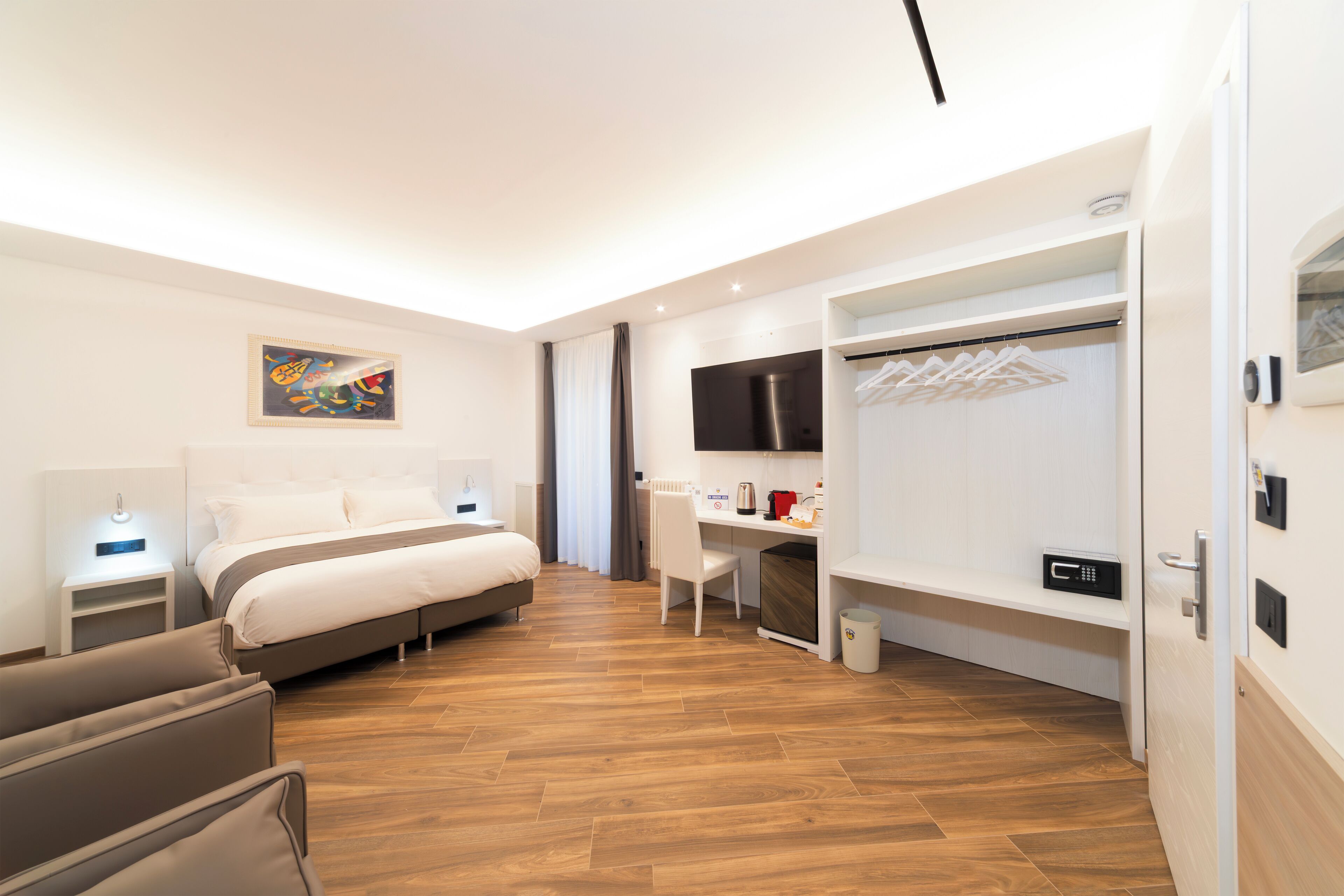 A modern hotel room with a bed, desk, chair, and a TV on the wall.
