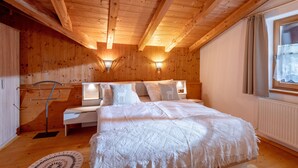 A wooden-paneled room with a bed, two bedside lamps, a radiator, and a window with curtains. - Apartment 'Lisa' with Mountain View, Balcony and Wi-Fi (Fügen)