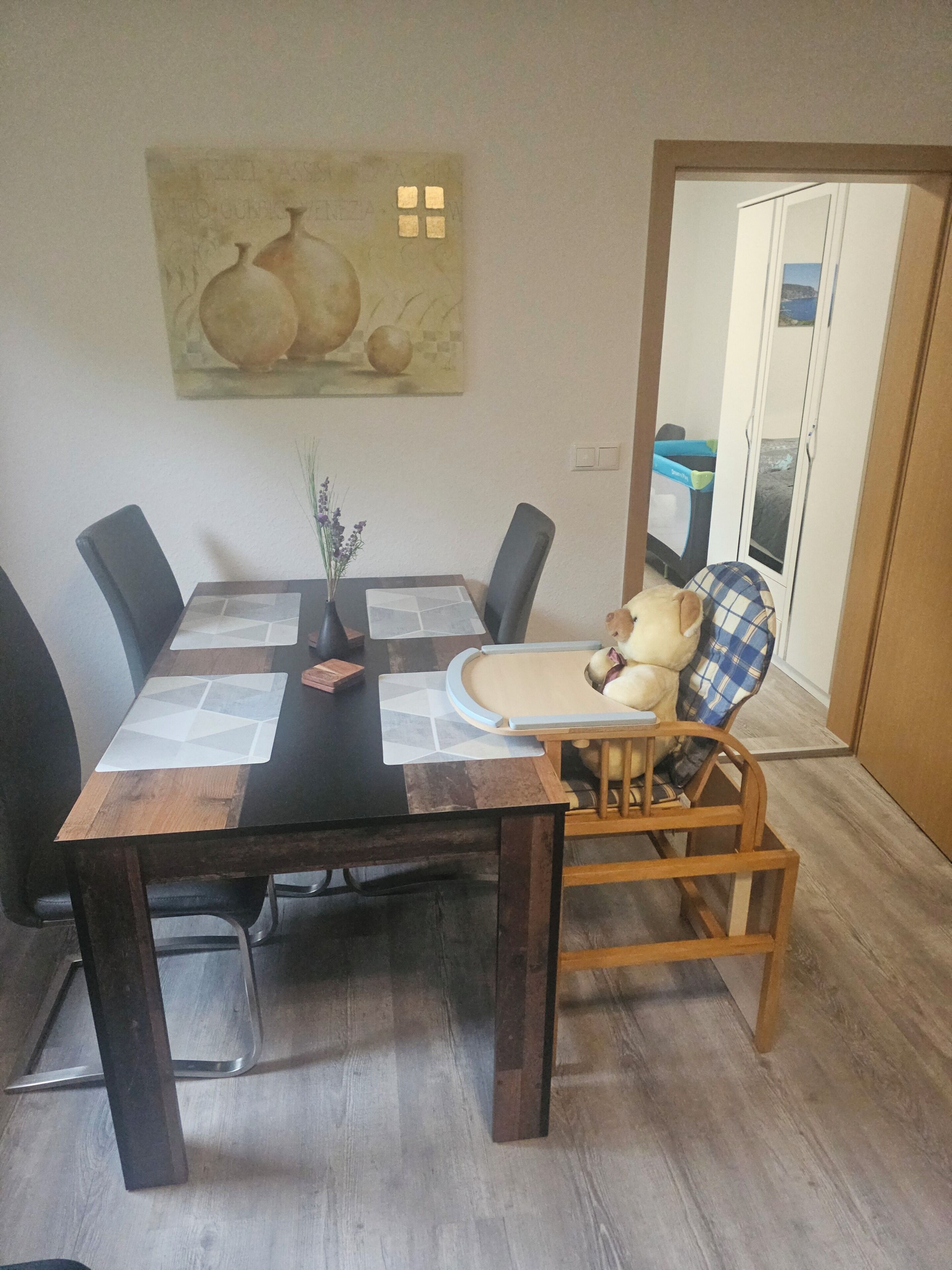 A dining area with a table, chairs, a vase with flowers, and a painting on the wall.