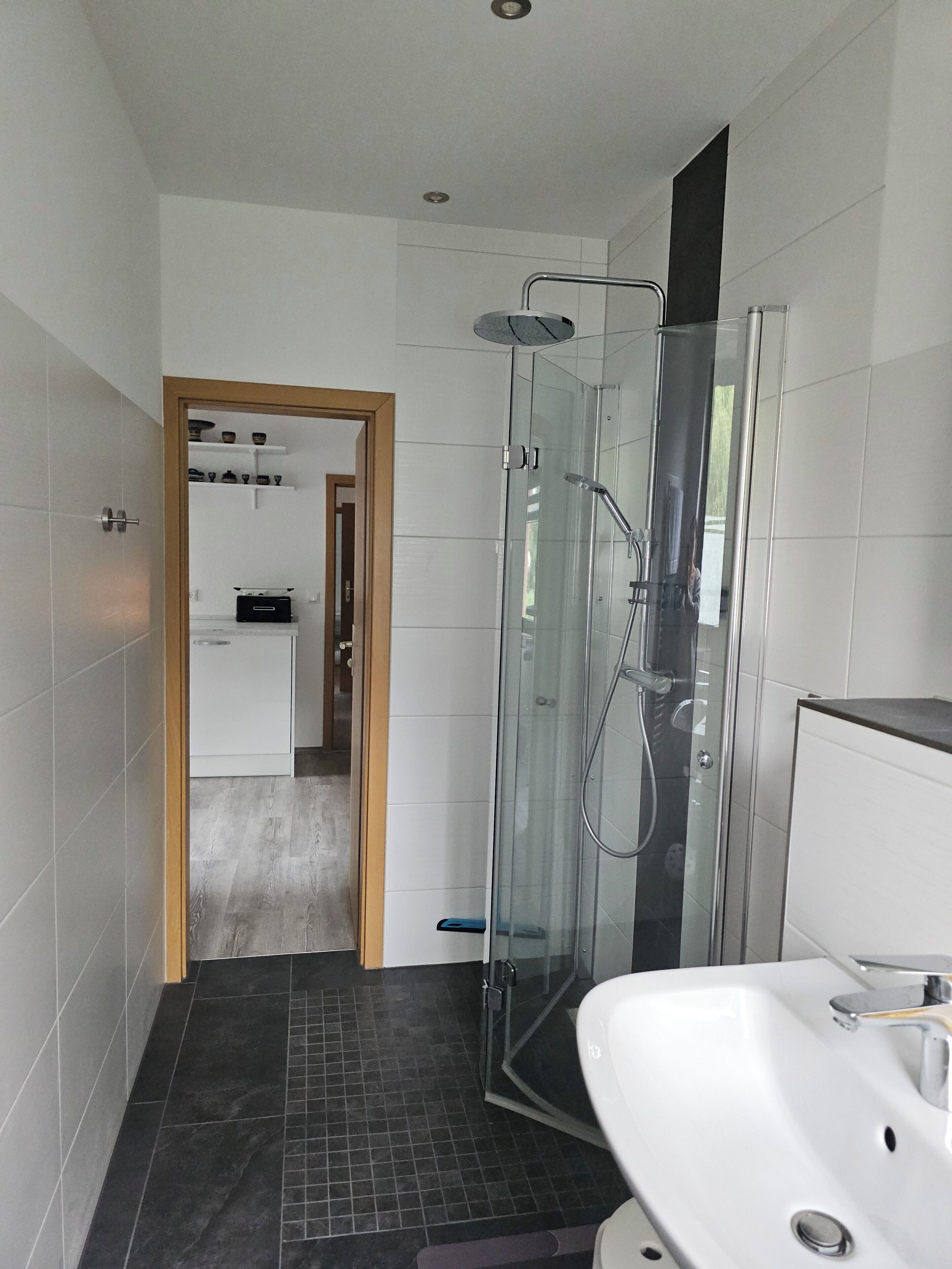 Ein modernes Badezimmer mit einer Glaskabine zur Dusche, einem weißen Waschbecken und einem gefliesten Boden.