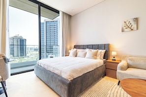 A modern hotel room with a large bed, a desk, and a view of the cityscape through the window.