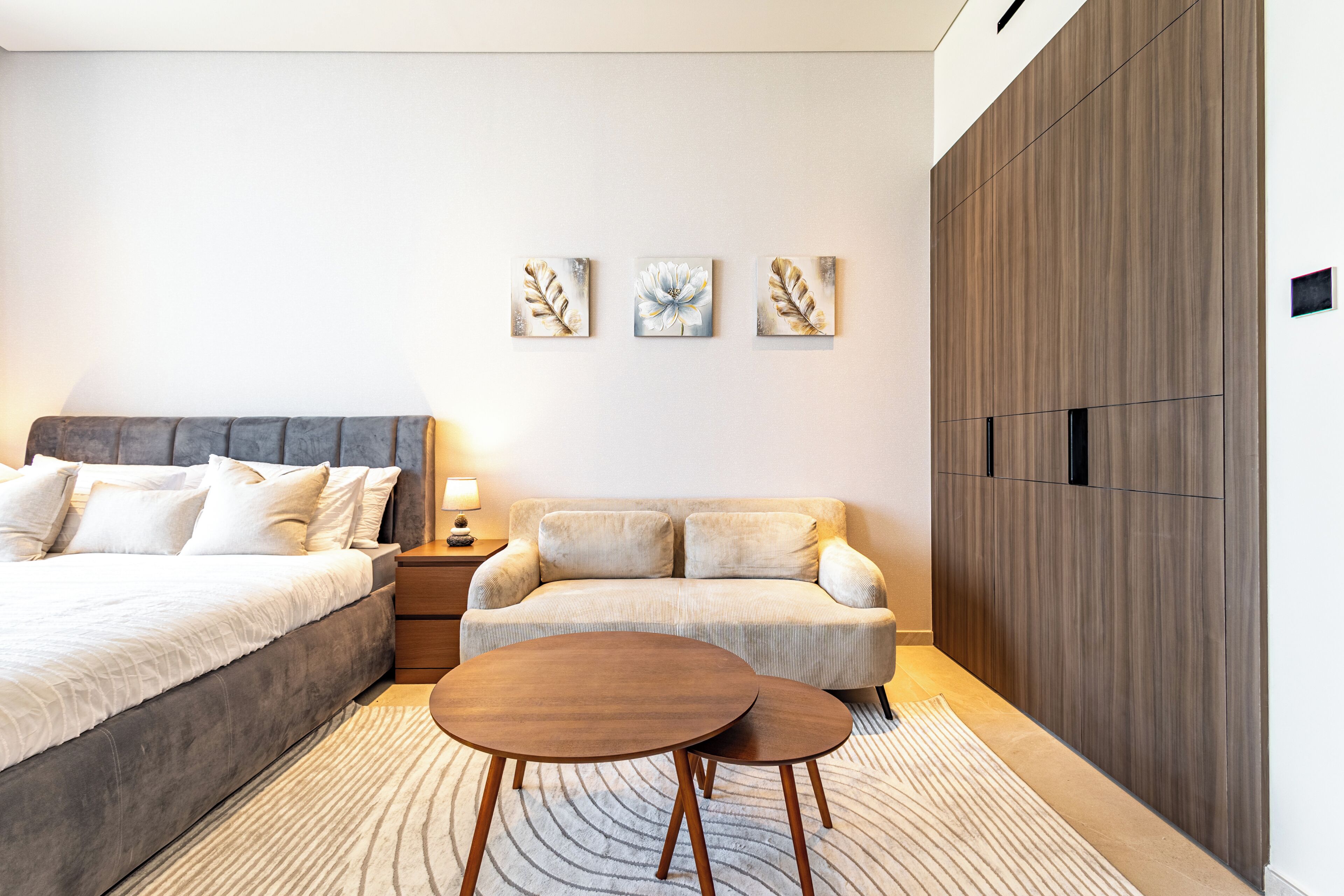 Une chambre moderne comprenant un lit, un canapé, une table de chevet, une lampe et trois tableaux accrochés au mur.