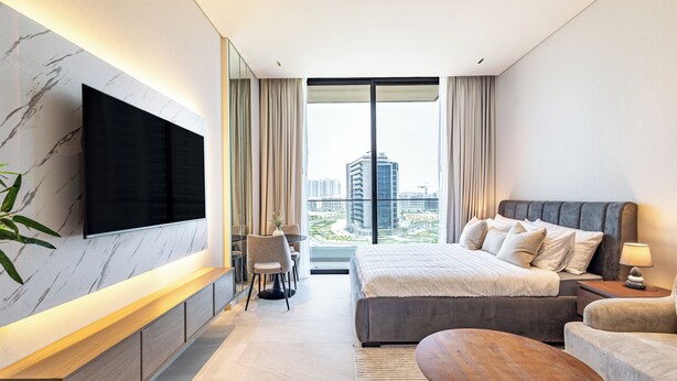 Ett modernt hotellrum med en stor säng, en tv som är monterad på väggen, en sittgrupp med ett bord och utsikt över stadsbilden genom stora fönster.