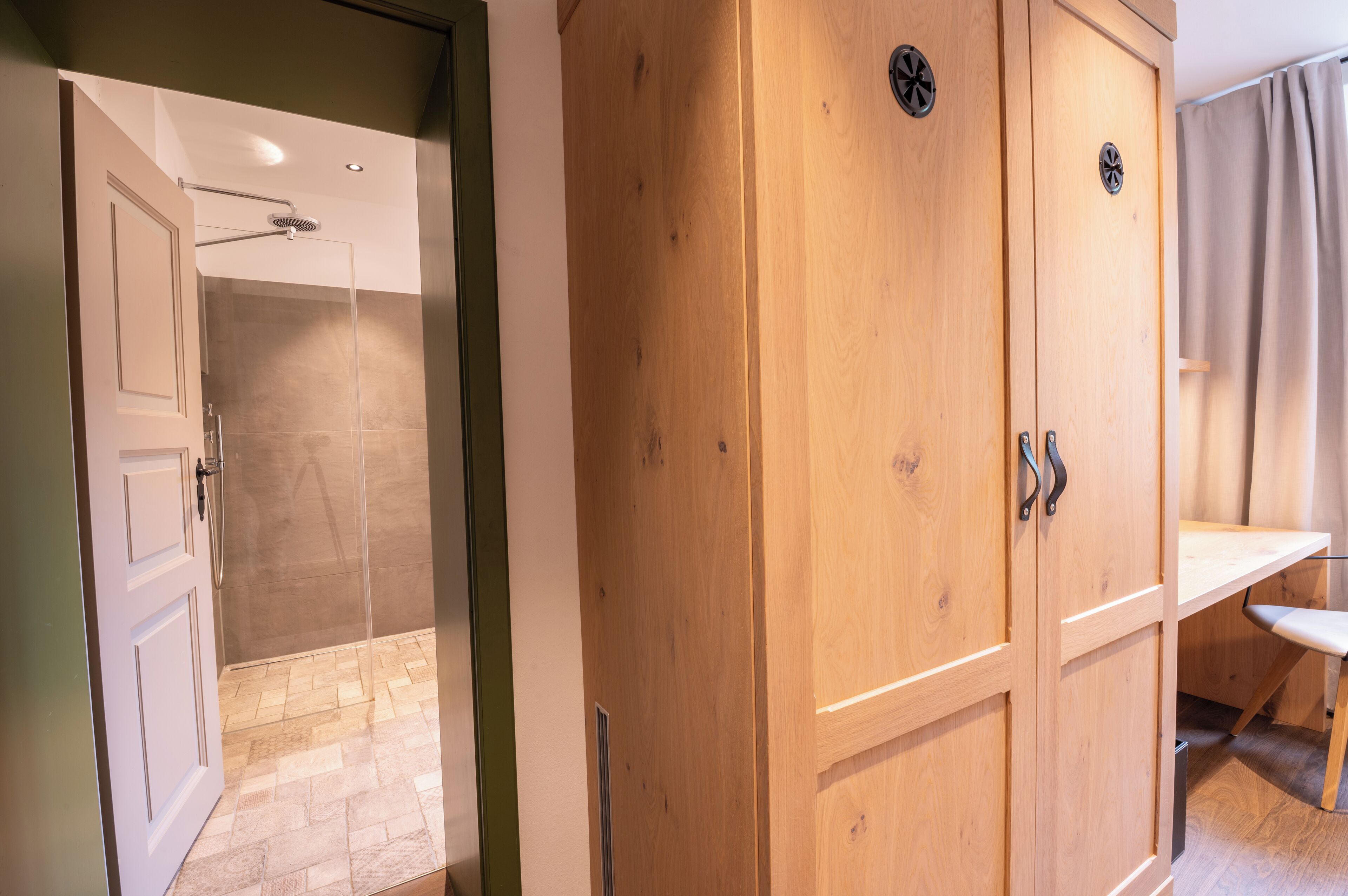 Un armario de madera con espejo, una zona de ducha con puerta de cristal y un banco de madera.