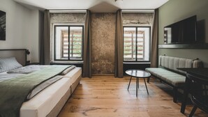 A room with a bed, a sofa, a TV, and two windows with shutters. - Landhotel Alte Zollstation (Pittenhart)