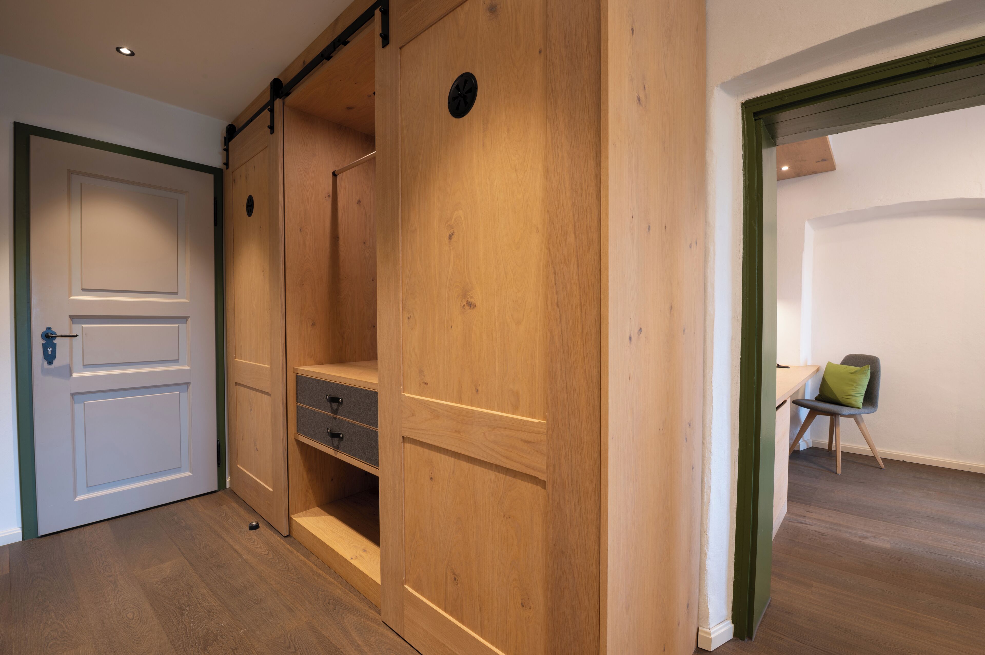 A room with a wooden wardrobe, a white door, and a desk with a chair.