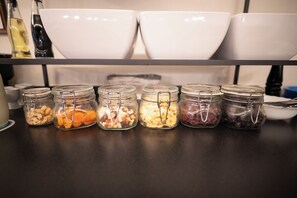 A kitchen counter with jars of nuts and dried fruits, white bowls, and a bottle of oil.