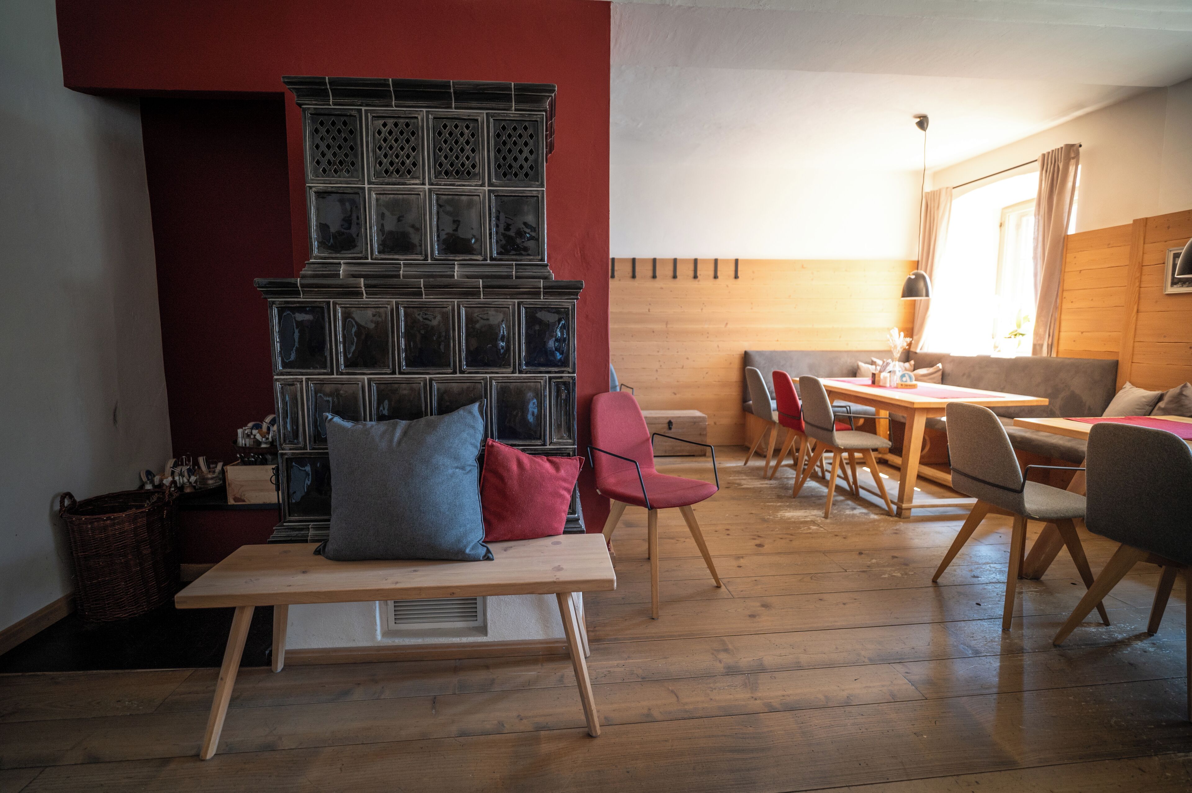 Una habitación acogedora con suelo de madera, una pared de acento roja, una chimenea, una zona de comedor con mesa y sillas, y una ventana con cortinas.
