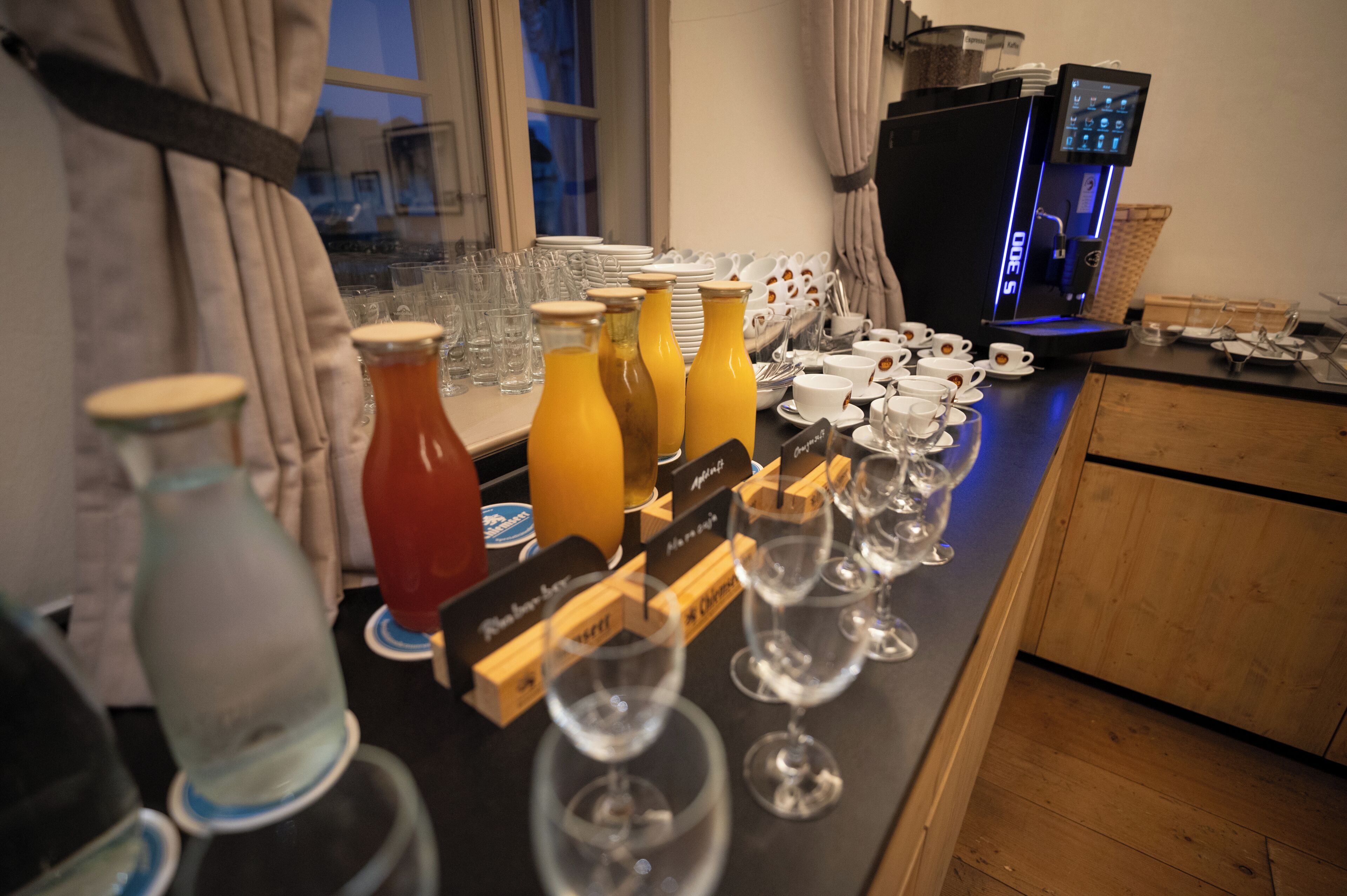 Una barra de desayuno con diversas bebidas, vasos y una máquina de café.