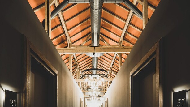 A hotel hallway with a red carpet, wooden walls, and a high ceiling with exposed beams. - Landhotel Alte Zollstation (Pittenhart)