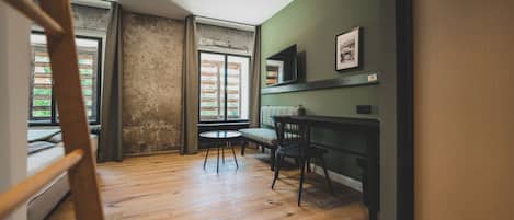 A room with a wooden floor, a dining table with chairs, a window with curtains, and a framed picture on the wall.