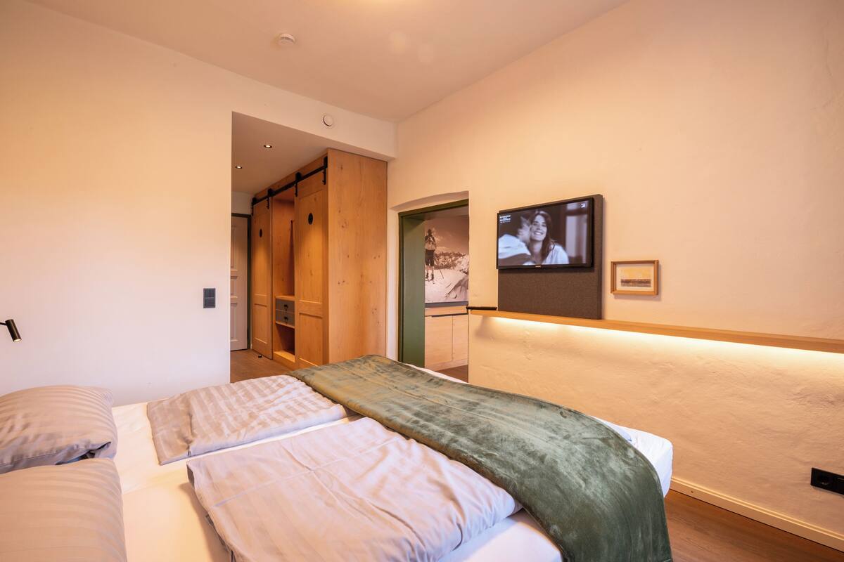A bedroom with two beds, a TV mounted on the wall, and a wooden wardrobe.