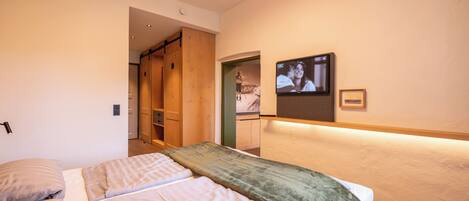 A bedroom with two beds, a TV mounted on the wall, and a wooden wardrobe.