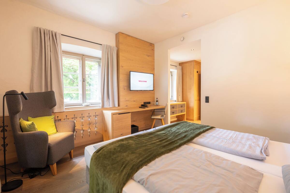 A modern hotel room with a bed, a desk, a chair, and a television displaying "WELCOME".