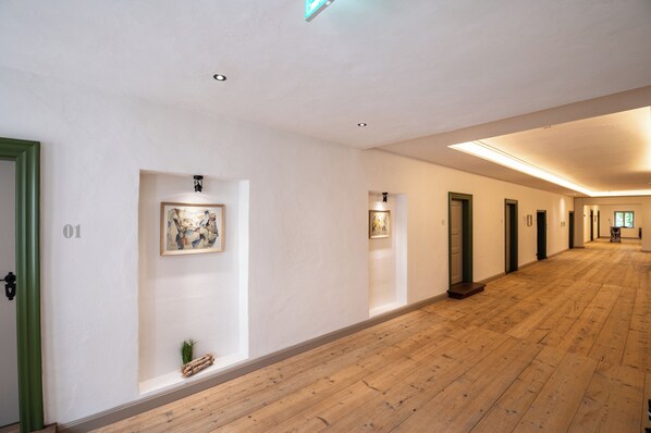 A long, narrow hallway with wooden flooring, white walls, and doors numbered 01 to 39.