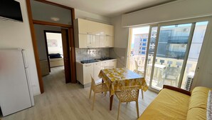 Un appartamento compatto con angolo cottura, zona pranzo con tavolo e sedie, divano e balcone con vista sulla città.