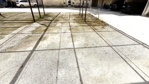 Un'area di parcheggio coperta con posti auto delimitati, identificati con B20 e B18, un pavimento in cemento e un edificio con un balcone sullo sfondo.