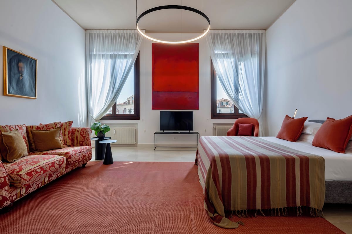 A modern hotel room with a sofa, a bed, a TV, and a large window with curtains.