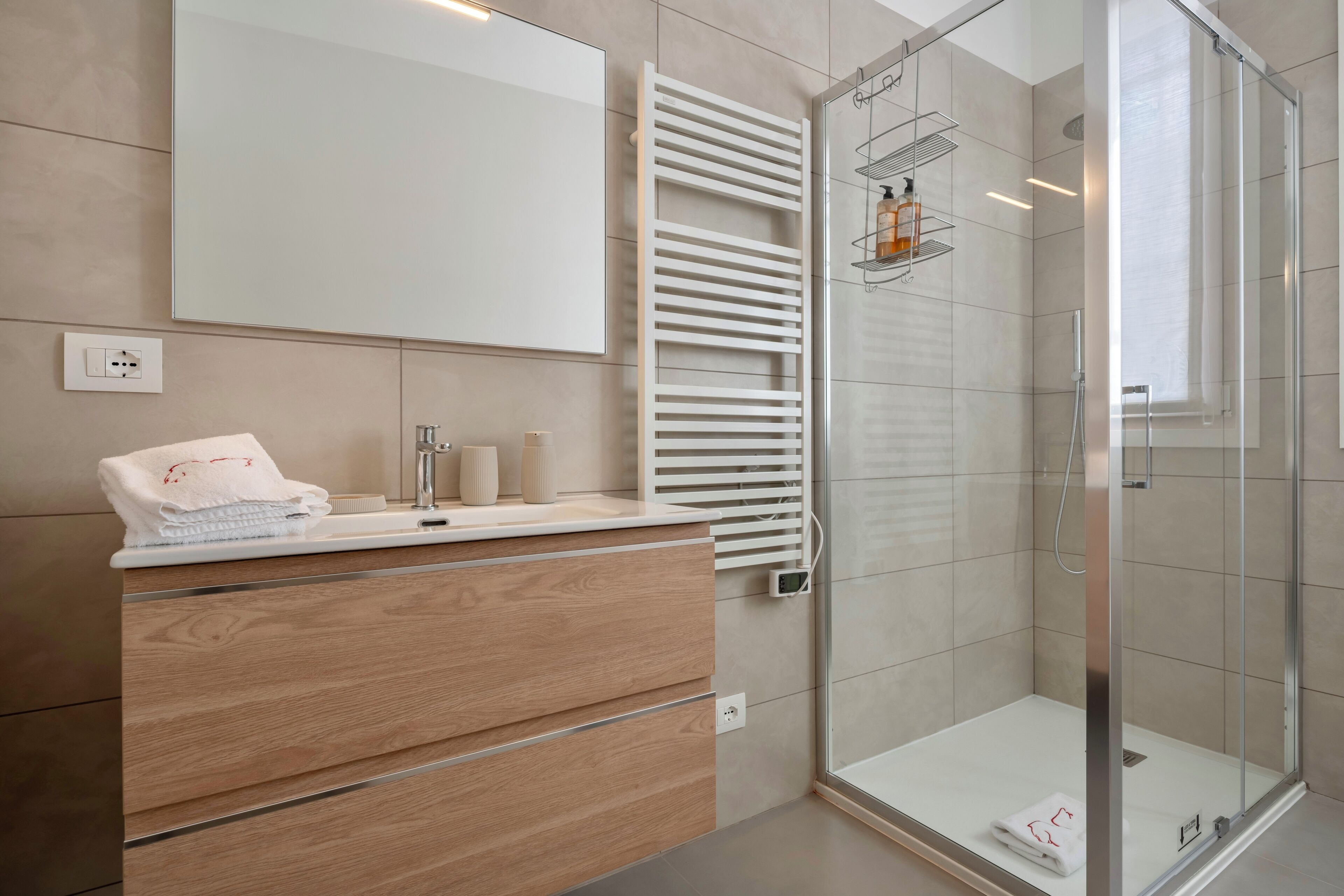 Un baño moderno con cabina de ducha de vidrio, tocador de madera, un espejo grande y una toalla sobre la encimera.