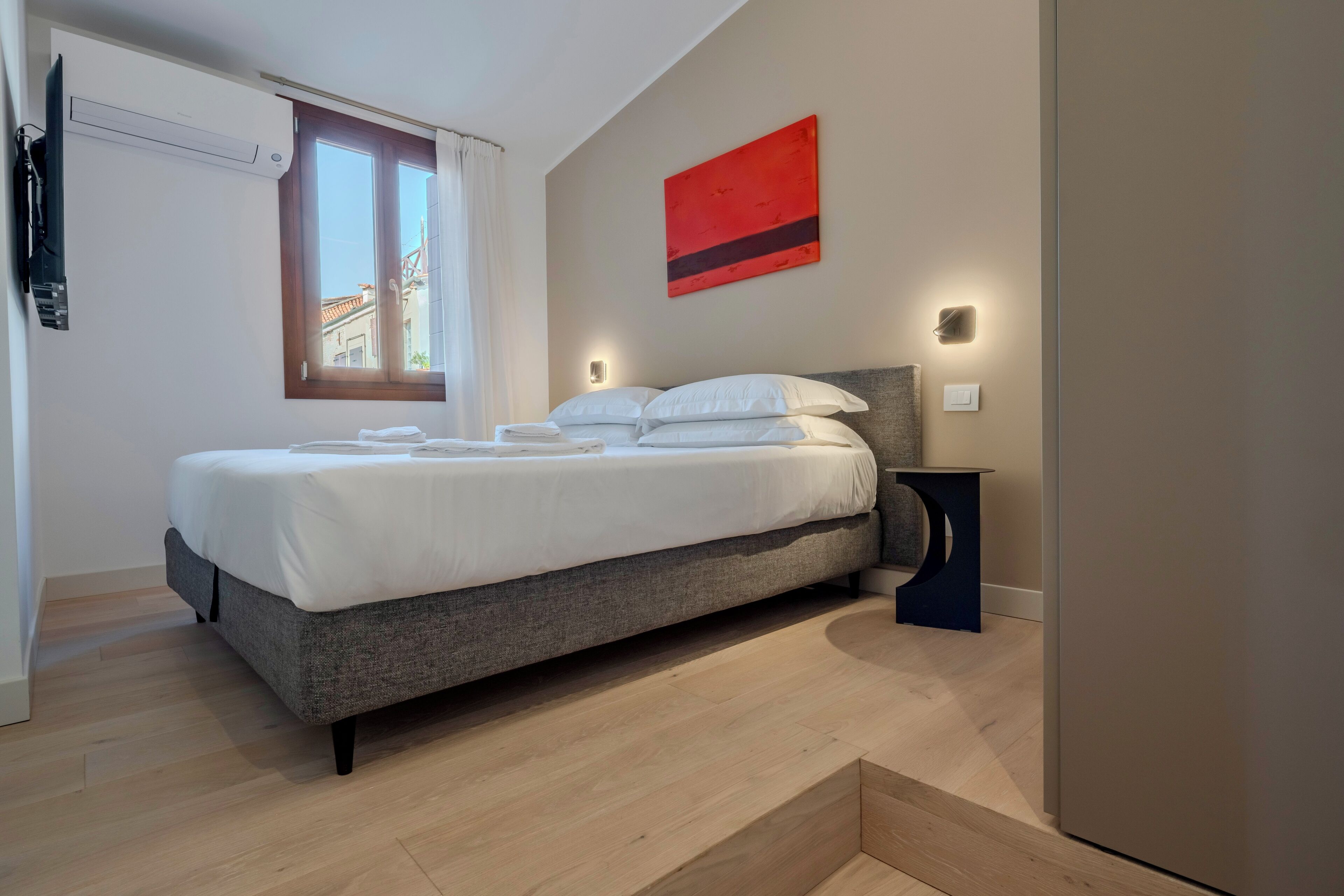Een moderne slaapkamer met een bed, nachtkastje, wandlamp en raam met gordijnen.