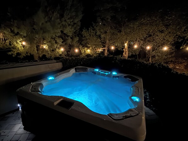 A hot tub with blue LED lights, surrounded by trees and string lights.