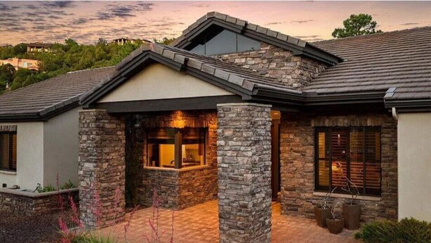 A modern house with stone pillars, a brick driveway, and a well-lit entrance. - Serene Luxe Prescott Pines Hideaway, Games + Epic Views, Sleep 16+, Fun For All! (Prescott)