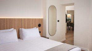 Ett hotellrum med en stor säng, en sänggavel i trä, en rund spegel och utsikt över matsalen.