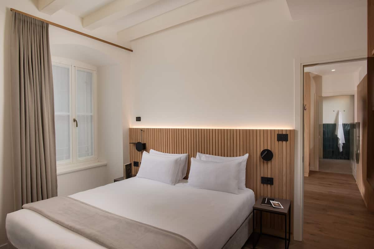 A modern hotel room with a large bed, a nightstand, a wall-mounted clock, and a window with curtains.