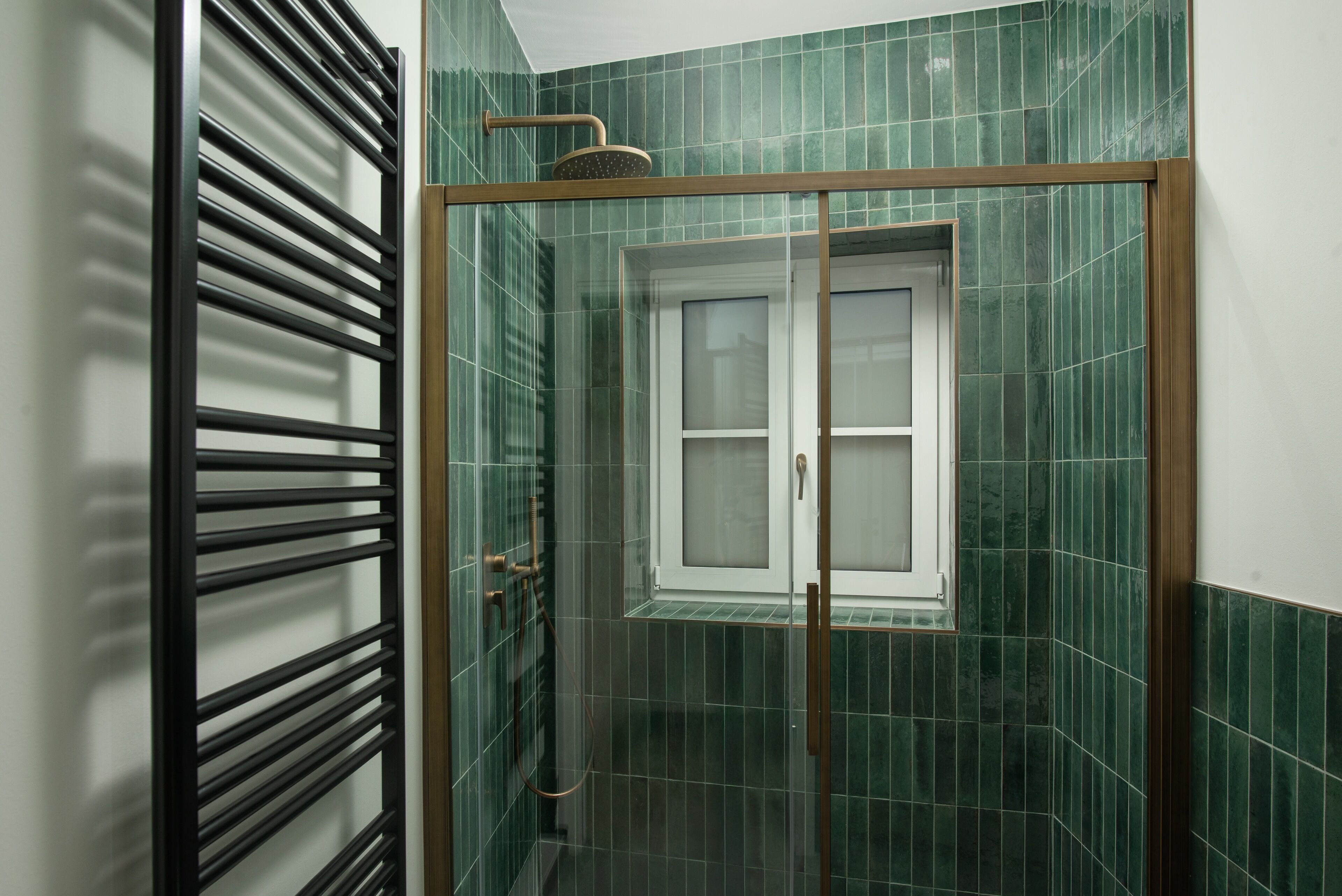 Een badkamer met een glazen deur, groene tegels en een douche met een houten hendel.