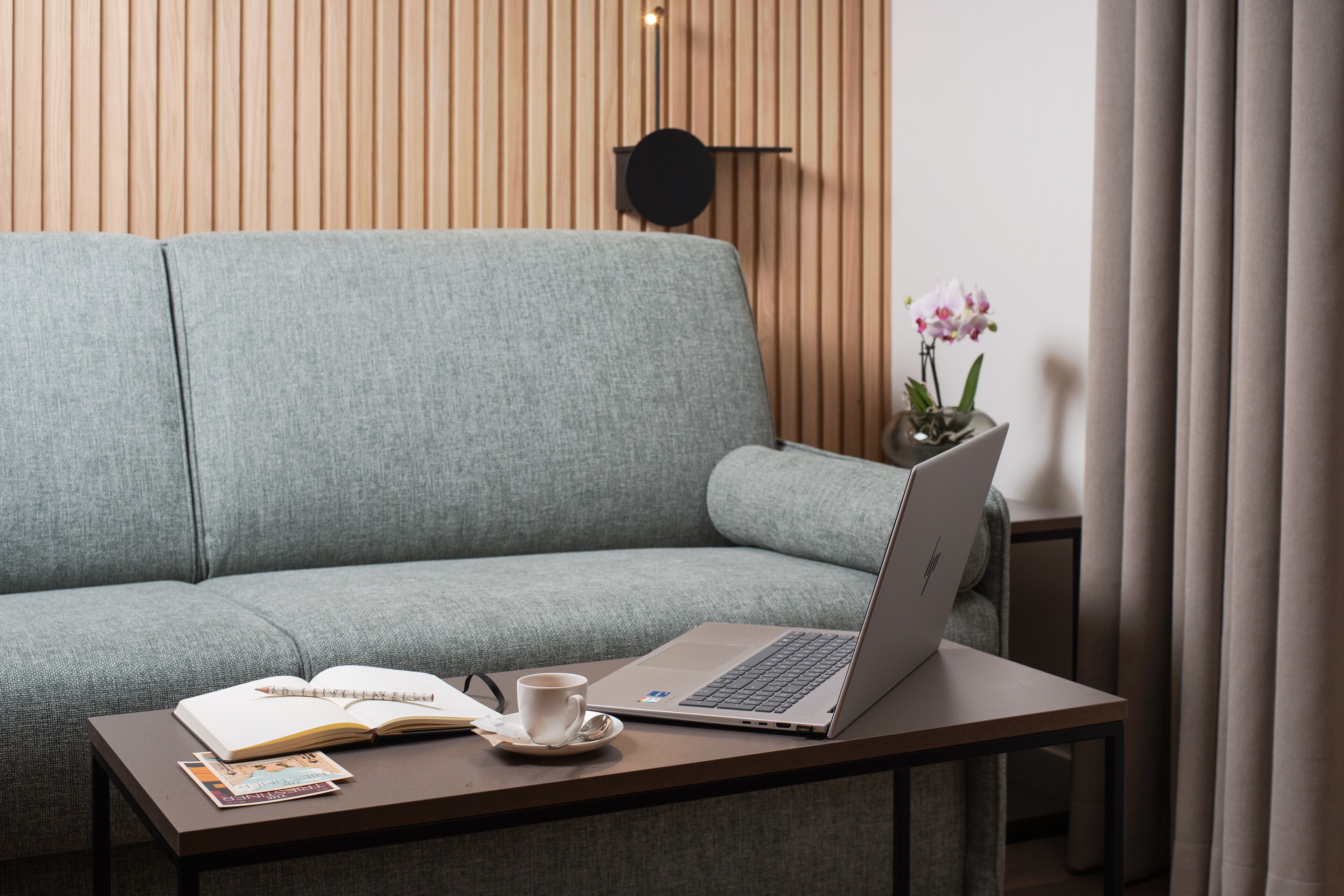 Una sala de estar moderna con un sofá gris, una mesa de centro con una computadora portátil, un libro y una taza.