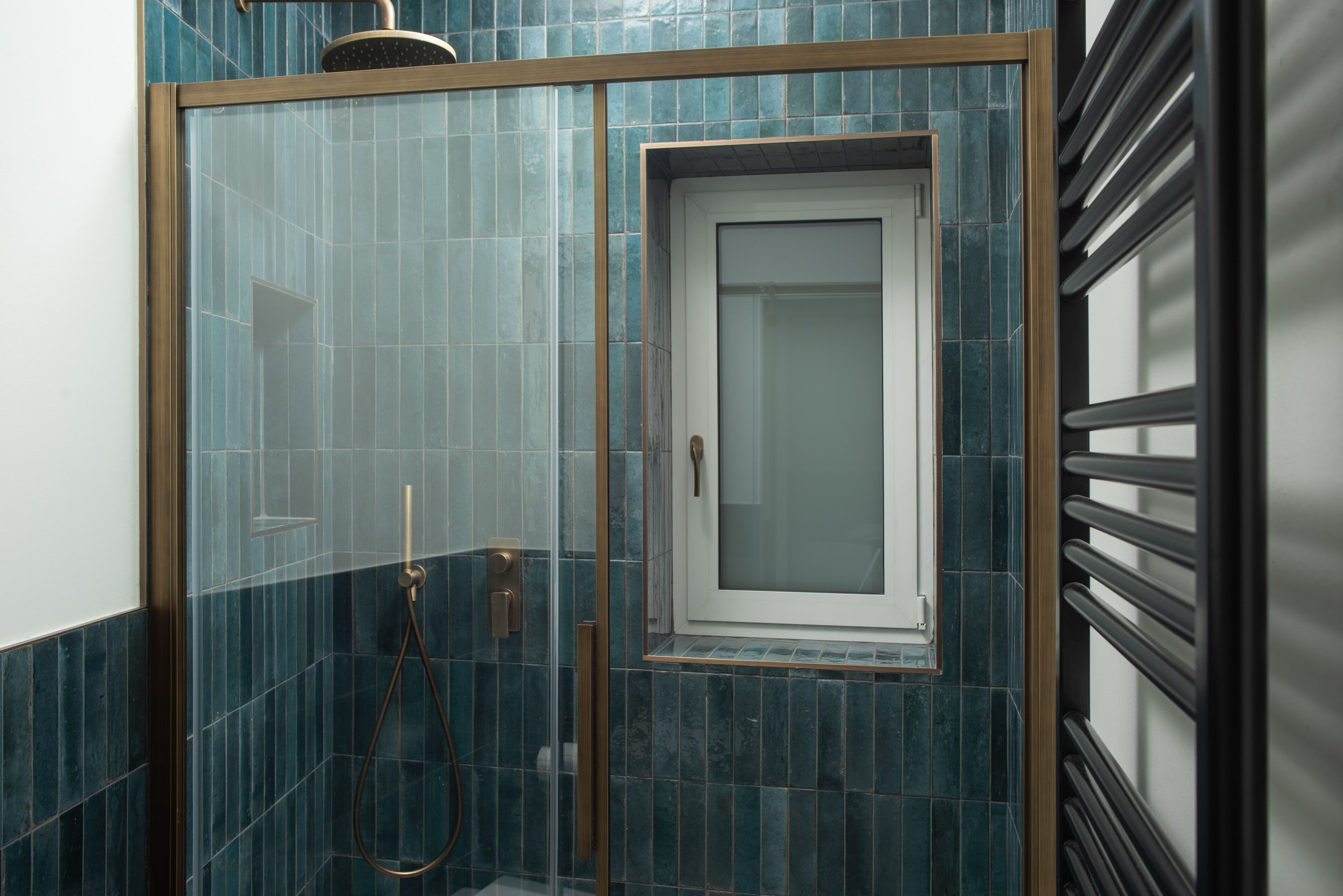 A shower with a glass door and a window, surrounded by blue-tiled walls.