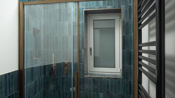 A shower with a glass door and a window, surrounded by blue-tiled walls.