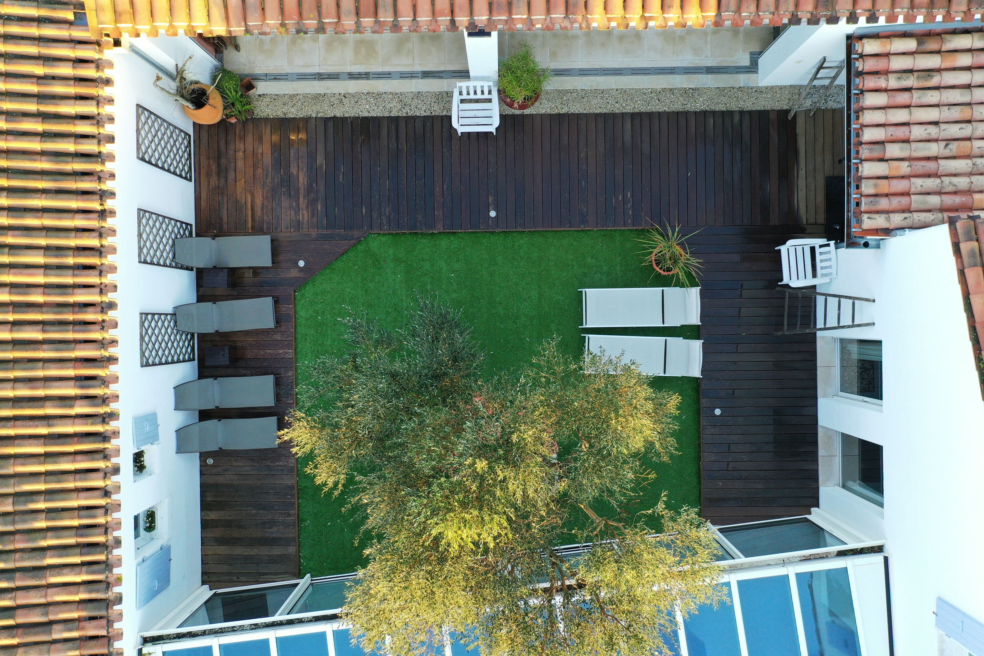 Vue aérienne d’une cour avec une pelouse verdoyante, une terrasse en bois et des plantes en pot.