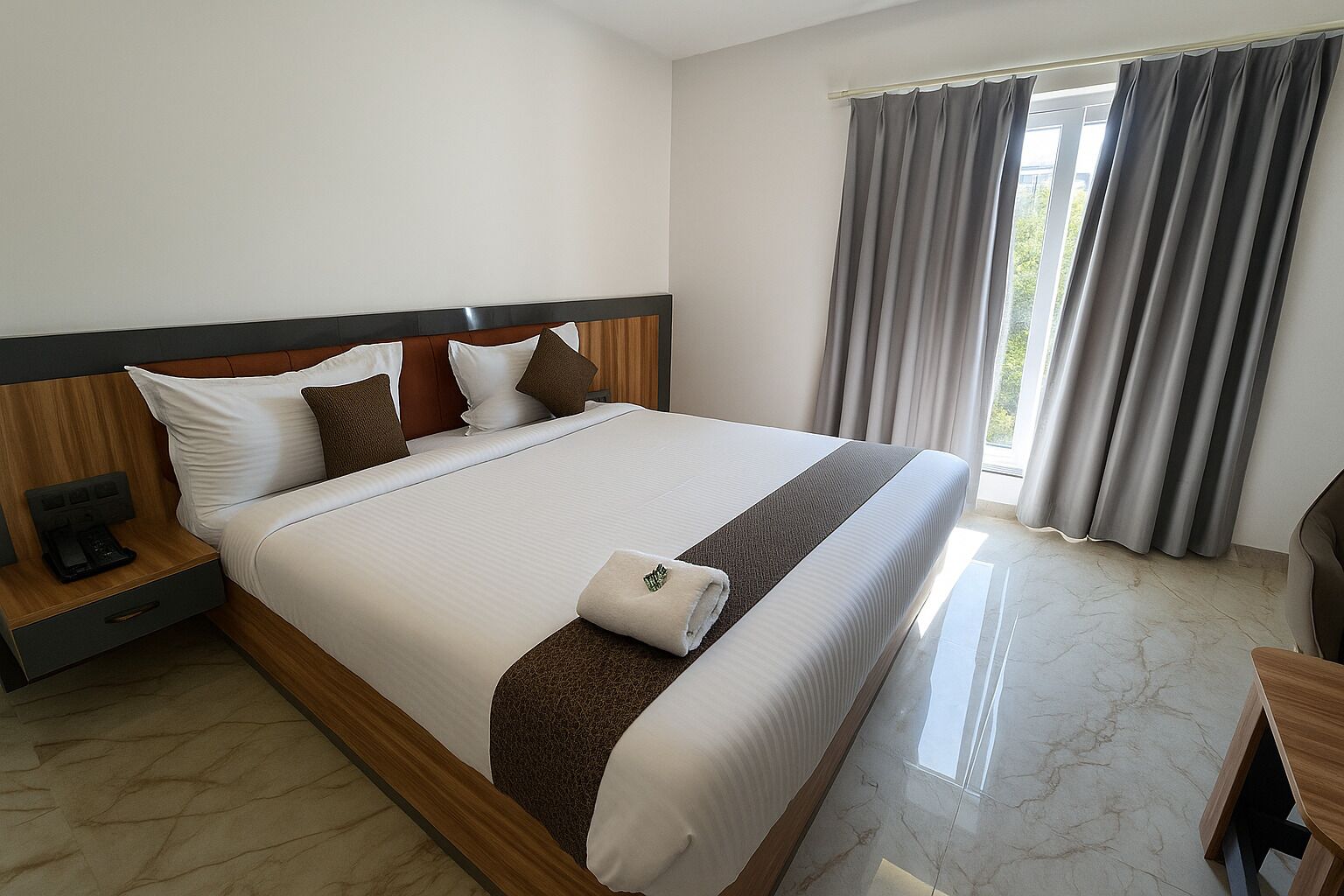 A modern hotel room with a large bed, wooden headboard, and a nightstand with a phone.