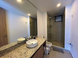 A modern bathroom with a granite countertop, two sinks, a toilet, and a glass-enclosed shower.