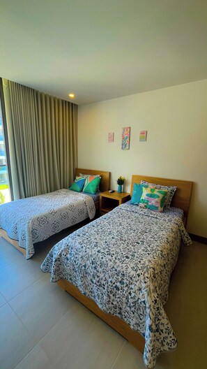 Habitación de hotel con dos camas, una mesita de noche y una ventana con cortinas.