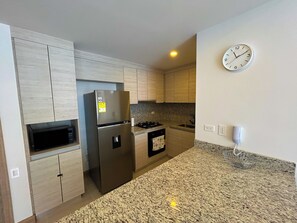 Una cocina moderna con armarios de madera clara, electrodomésticos de acero inoxidable, encimeras de granito y un reloj de pared.