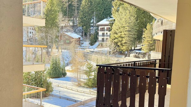 A view from a balcony with a wooden railing, overlooking a snowy landscape with trees and buildings. - "Madesimo Ski Suite": apartment just steps from the slopes! (Madesimo)